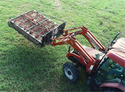Aerial view of a red tractor in a green field with a bale grabber on the front end loader