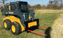 Deere skid steer with 2 red bale spears on the front