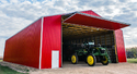 Large red pole barn trimmed in white with a John Deere implement under the open Exterior Bi-Fold Door