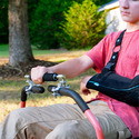 A young man with his left arm in a sling using a Zero-Turn Mower One-Hand Steering Bar to guide a zero-turn mower